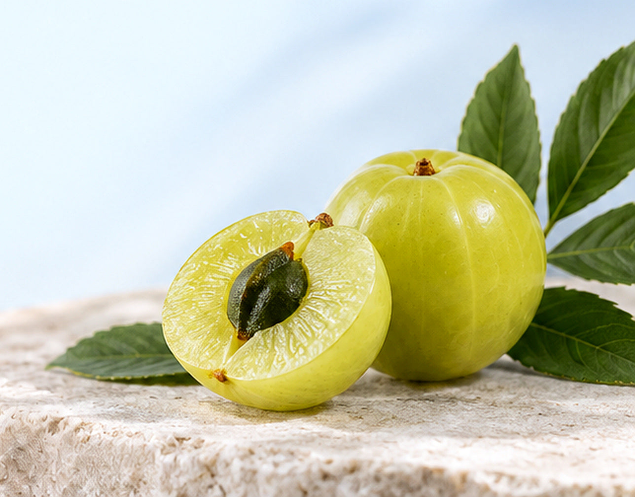 Close-up of whole and cut amla fruit with leaves on stone